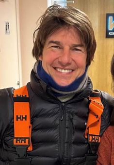 a smiling man wearing an orange and black vest with his neck braces around his neck