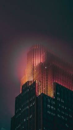 the top of a tall building lit up in red, yellow and orange lights at night