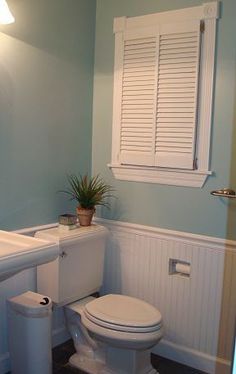 a white toilet sitting in a bathroom next to a window with shutters on it