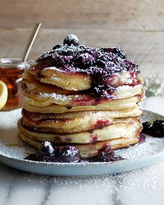 a stack of pancakes covered in blueberries and powdered sugar on a plate next to a cup of tea