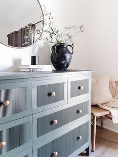 a black vase sitting on top of a blue dresser next to a mirror and chair