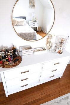 a white dresser topped with lots of drawers under a round mirror