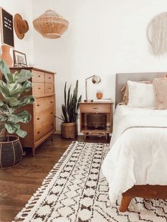 a bedroom with a bed, dresser and plants on the side table in front of it