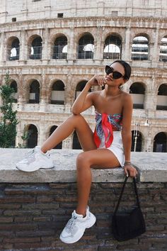 a woman is sitting on a ledge in front of the colossion with her purse