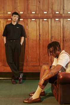 two young men sitting on the floor in front of wooden lockers, one with his foot up