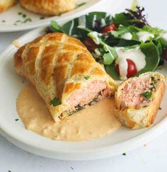 two white plates topped with pastries covered in meat and sauce next to a salad