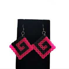 a pair of pink and black beaded earrings sitting on top of a black stand