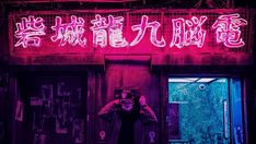 a man standing in front of a building with neon lights on it's side