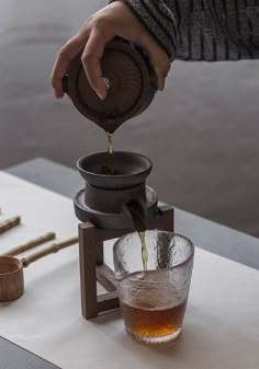 a person pouring tea into a glass on top of a table