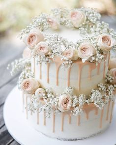 a wedding cake decorated with flowers and drizzled in icing on a wooden table