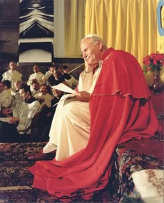 an old man sitting in front of a group of people wearing red and white robes