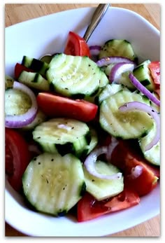 a white bowl filled with sliced cucumbers and onions on top of a wooden table