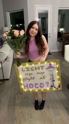 a woman holding a sign that says light up my house at hoco? with flowers in front of her