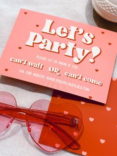 a pair of red glasses sitting on top of a table next to a card with the words let's party