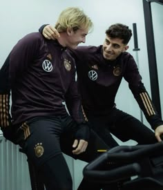 two young men sitting on top of an exercise bike