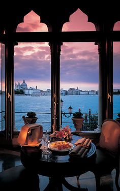 a table with food on it in front of large windows overlooking the water at sunset