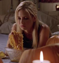 a woman laying on the floor eating spaghetti from a bowl next to a lit candle