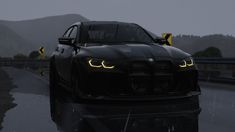 the front end of a black car on a wet road with mountains in the background