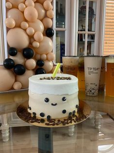 a birthday cake sitting on top of a glass table next to balloons and a cup