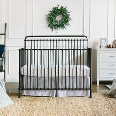 a baby crib in a white room with a wreath on the wall above it