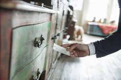 a person holding a piece of paper in front of an old wooden dresser with drawers