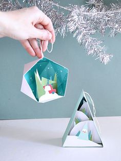 someone holding an ornament in front of a christmas tree with snow on it