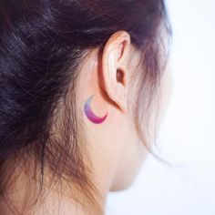 a woman's ear with a small crescent tattoo on the back of her left ear