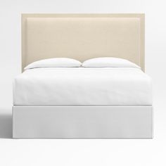 a bed with white sheets and pillows on top of it's headboard, in front of a light colored wall