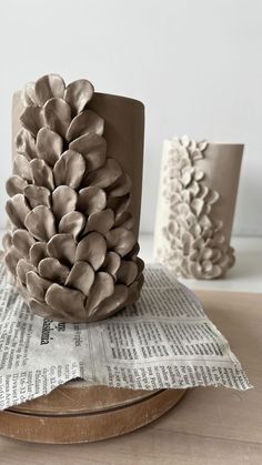 a ceramic pine cone sitting on top of a newspaper next to two other vases