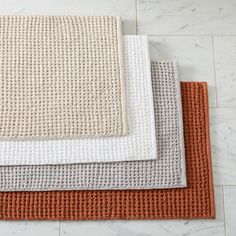 three different colored rugs sitting on top of a white tile floor next to each other