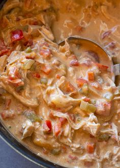 a ladle full of chicken and vegetable chowder in a pot with a spoon