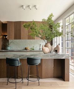 two stools sit in front of an island with marble countertops and wooden cabinets