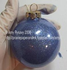 a hand holding a blue christmas ornament in it's gloved hands