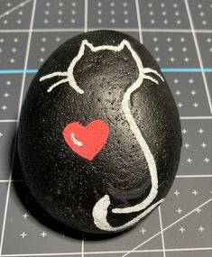 a black rock with a red heart painted on it's face and the shape of a cat