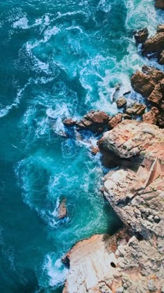 an aerial view of the ocean with rocks and blue water in the foreground, from above