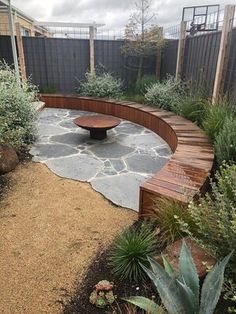 a wooden bench sitting in the middle of a garden next to a stone walkway and fence