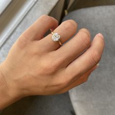 a woman's hand with a diamond ring on her left hand, next to a window