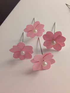 four pink flowers with pearls on them sitting on a white table next to some scissors