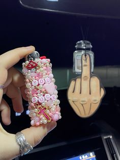 a person holding up a cell phone case made out of beads and other things in the background