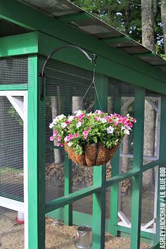 a green chicken coop with flowers hanging from the roof