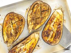 four cooked eggplant halves on a baking sheet with a spatula next to them