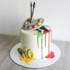 a cake decorated with paint and brushes on top of a white plate that is sitting on a wooden table