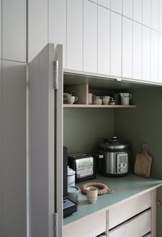 an open cabinet in a kitchen with pots and pans on the counter top, next to a crock pot