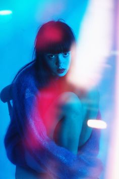 a woman sitting on a chair in front of a blue and red background with blurry lights