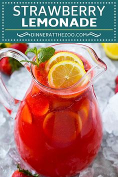 a pitcher filled with red liquid and sliced lemons on top of ice next to strawberries