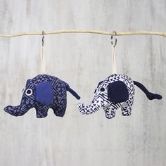 two stuffed elephants hanging from clothes pins on a line with strings attached to them, one is blue and the other is white