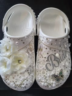 a pair of white baby shoes with flowers and pearls on the bottom one shoe has a butterfly