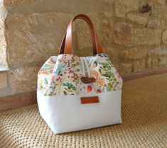 a white purse with flowers on it sitting next to a stone wall