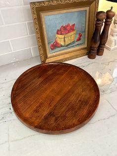 a wooden cutting board sitting on top of a counter next to a painting and candle holder