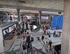 many people are walking up and down the escalator in an indoor area with signs above them